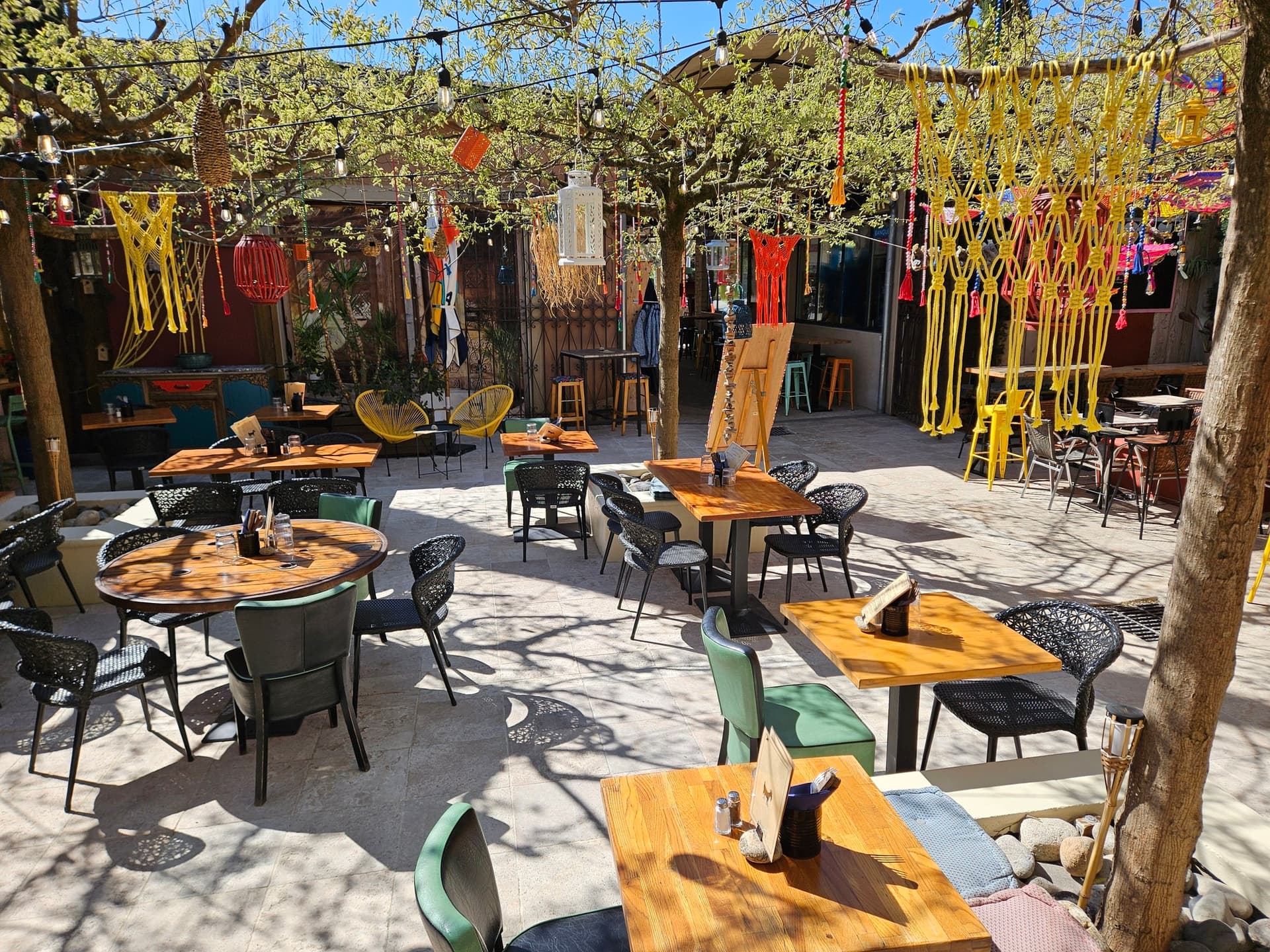 Terrasse du Quésaco décorée de macramés colorés suspendus aux arbres